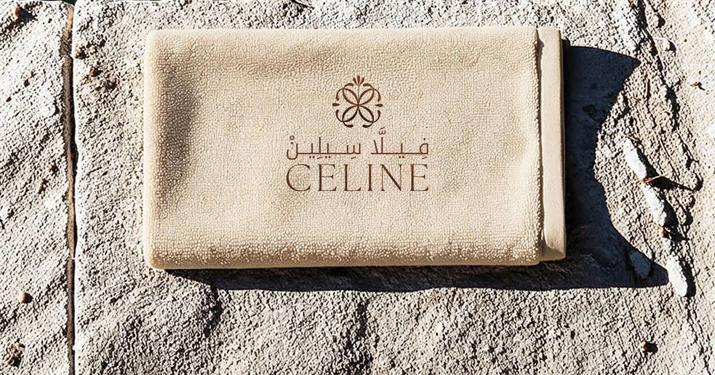A folded sand-coloured towel bearing the Villa Celine logo, on rough grey stone.