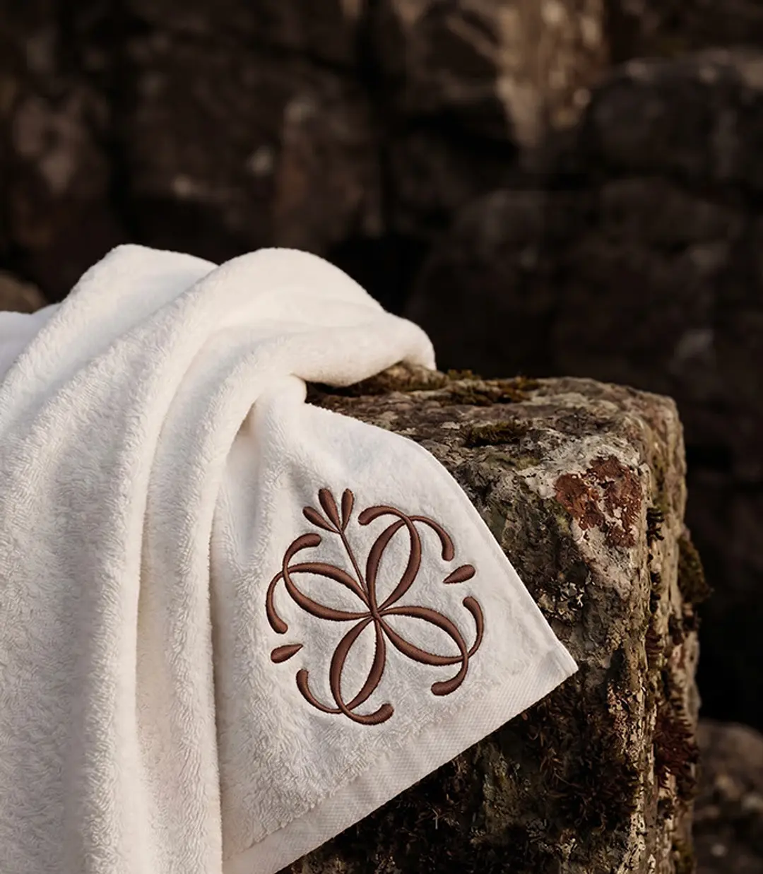 A soft white towel embroidered with the Celine mark, draped over dark stone.